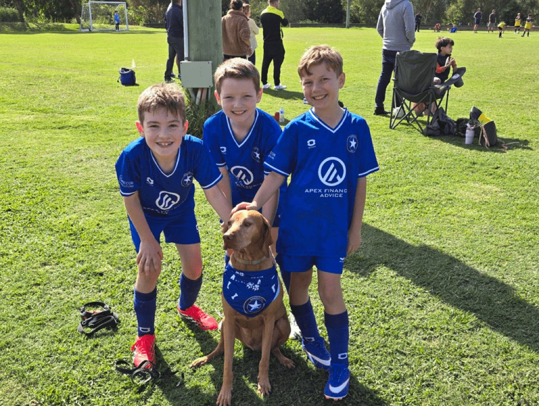 Junior footballers in Apex Financial Advice shirts with a dog on the sideline